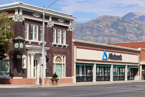 The Alta Bank building in Utah: a historic brick bank with a clock on the corner next to the modern Altabank branch, with mountains behind