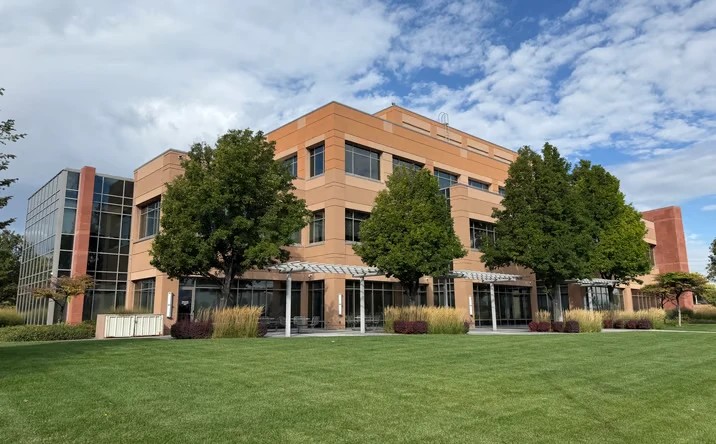 The Optum office building in Utah: a three-story building in warm brick tones with a lawn and mature trees in front